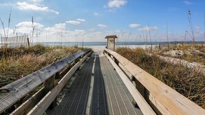 Ein hölzerner Steg führt zu einem Strand mit einer kleinen Schutzhütte.