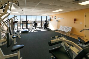 Un gimnasio con equipamiento de ejercicio, una banca y amplias ventanas con vistas.