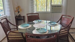 A dining area with a glass table surrounded by wicker chairs, a vase with flowers, and a window with bamboo view. - House of Aloha Retreat (Pahoa)