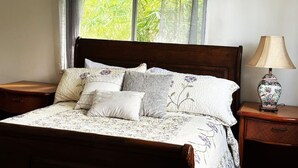 A bed with floral bedding, a wooden headboard, and a nightstand with a lamp. - House of Aloha Retreat (Pahoa)