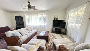 A living room with a sofa set, a television, and a ceiling fan. - House of Aloha Retreat (Pahoa)