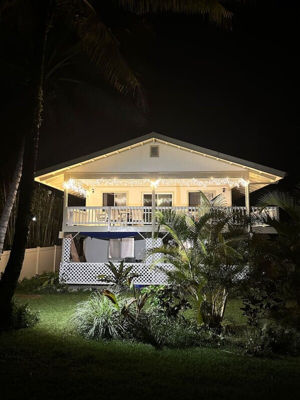 Een tweelaags huis met een overdekte veranda, witte hekwerk en lichtjes.