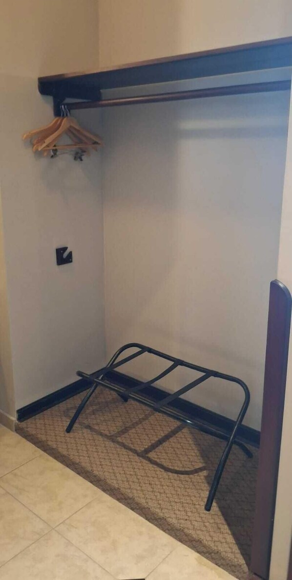 A small, enclosed room with a metal bed frame, a wooden hanger rack, and a small shelf.