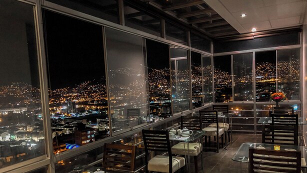 A high-rise restaurant with large windows offering a city view at night.