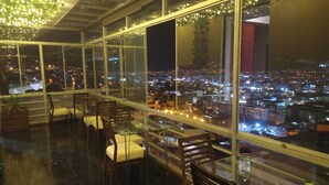 A high-rise restaurant with a panoramic city view, large windows, and modern furnishings.
