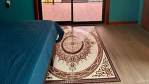 Una stanza con un'ampia porta-finestra scorrevole che si apre su un balcone, un letto con copriletto blu e un tappeto decorato.