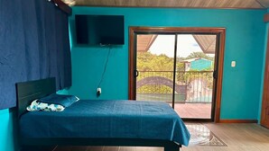 Una camera da letto con un letto, una TV fissata al muro e una porta scorrevole in vetro che dà su uno spazio all'aperto.