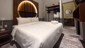 Una habitación de hotel moderna con una cama grande, cabecera de madera, armario empotrado y baño con espejo y lavamanos.