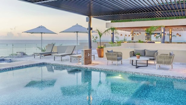 Un área de piscina moderna al aire libre con sillones de descanso y sombrillas, con vistas al mar.
