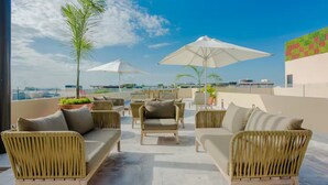 Una terraza en la azotea con mobiliario de mimbre, sombrillas y plantas en macetas.