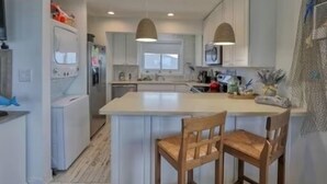 A modern kitchen with white cabinetry, a central island with two wooden chairs, pendant lighting, and a microwave above the island.