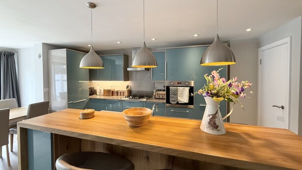 Una cucina moderna con mobili blu scuro, un'isola in legno con due sgabelli da bar, luci a sospensione e un vaso di fiori.