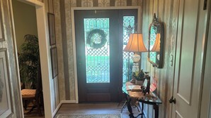 A hallway with a wooden floor, a patterned rug, a door with a decorative glass panel, and a wall-mounted lamp. - Charming 3-bedroom home in quiet Bryan neighborhood in the heart of AggieLand! (Bryan)