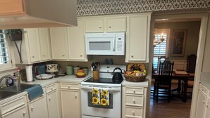 A kitchen with white cabinets, a microwave, a stove, and a sink. There is a basket of snacks on the stove and a window with blinds in the background. - Charming 3-bedroom home in quiet Bryan neighborhood in the heart of AggieLand! (Bryan)