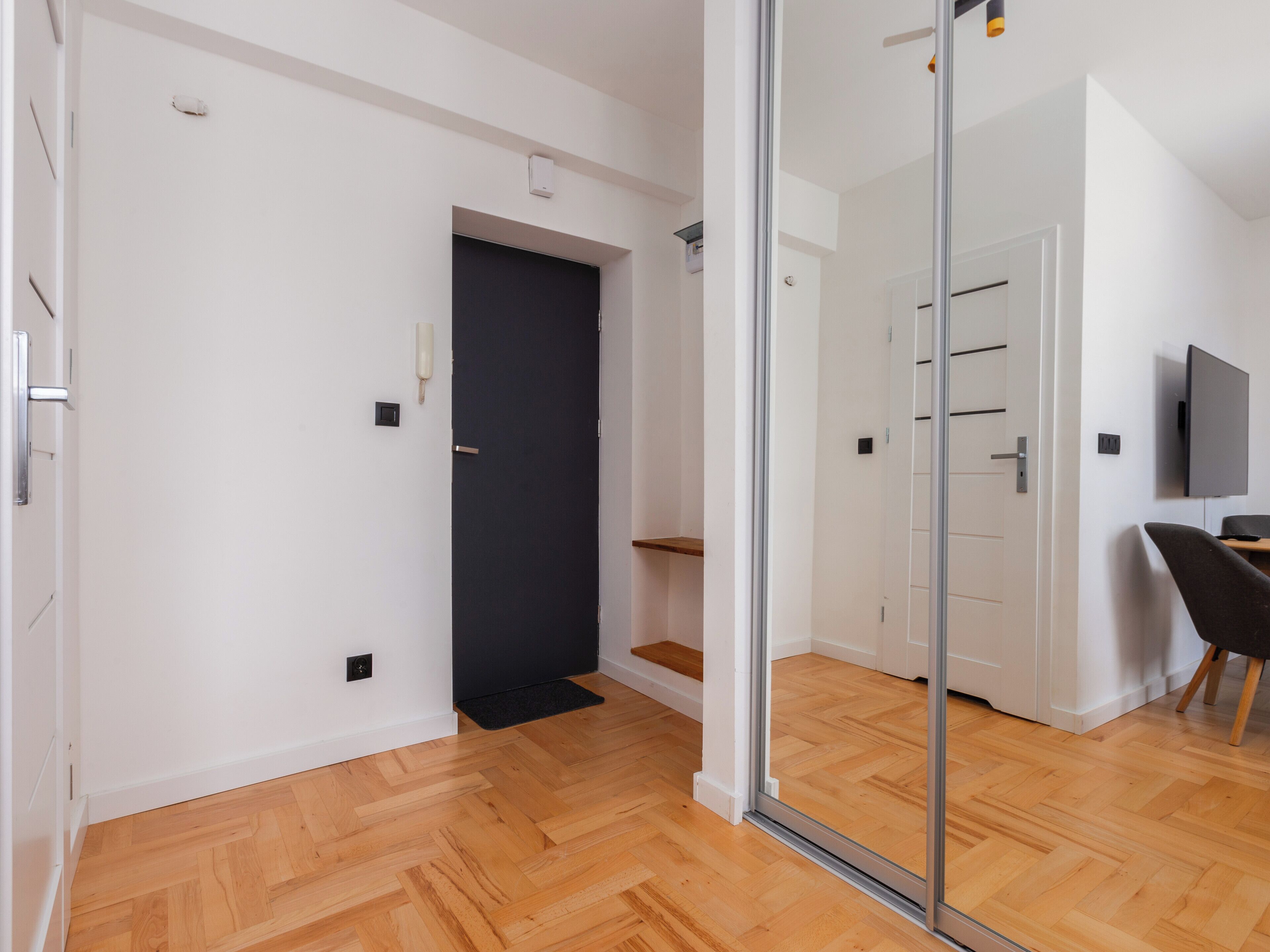 Un intérieur moderne avec un plancher en bois, une porte noire et une cloison en verre.