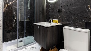 Un baño moderno con cabina de ducha acristalada, tocador con espejo y un inodoro.