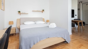 Un dormitorio moderno con cama, mesitas de noche, un escritorio y una silla. Se observan dos estantes montados en la pared con plantas.