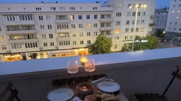 Un balcón con una mesa preparada para comer, con vistas a un paisaje urbano con edificios y una calle.