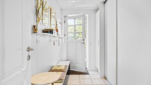 Un couloir avec une porte blanche, un banc et une petite table.