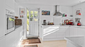 Une cuisine moderne avec des meubles blancs, un four encastré, une machine à café et divers ustensiles de cuisine.