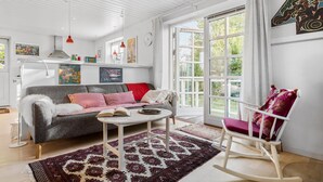 Un salon lumineux avec un canapé gris, un fauteuil à bascule blanc et un tapis à motifs.