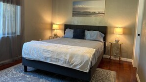 A bedroom with a bed, two bedside lamps, a painting on the wall, and a window with curtains. - Blue Beach Pool House-Port Orange/Daytona (Port Orange)