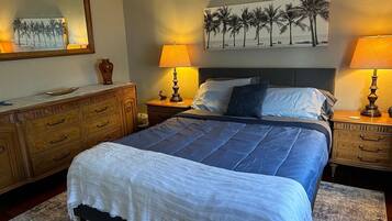 A bedroom with a large bed, two bedside tables with lamps, a dresser, a mirror, and a beach-themed painting on the wall.