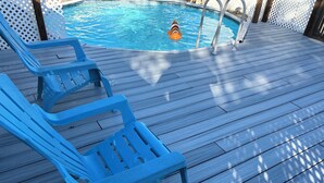 A wooden deck with blue plastic chairs and a pool with a dolphin float. - Blue Beach Pool House-Port Orange/Daytona (Port Orange)