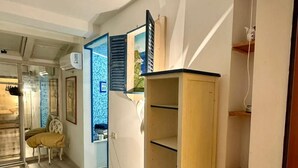A room with a wooden cabinet, a chair, and a mirror reflecting a blue wall and a window. -  L'affittacamere nel parco "Appia Antica" (Rome)