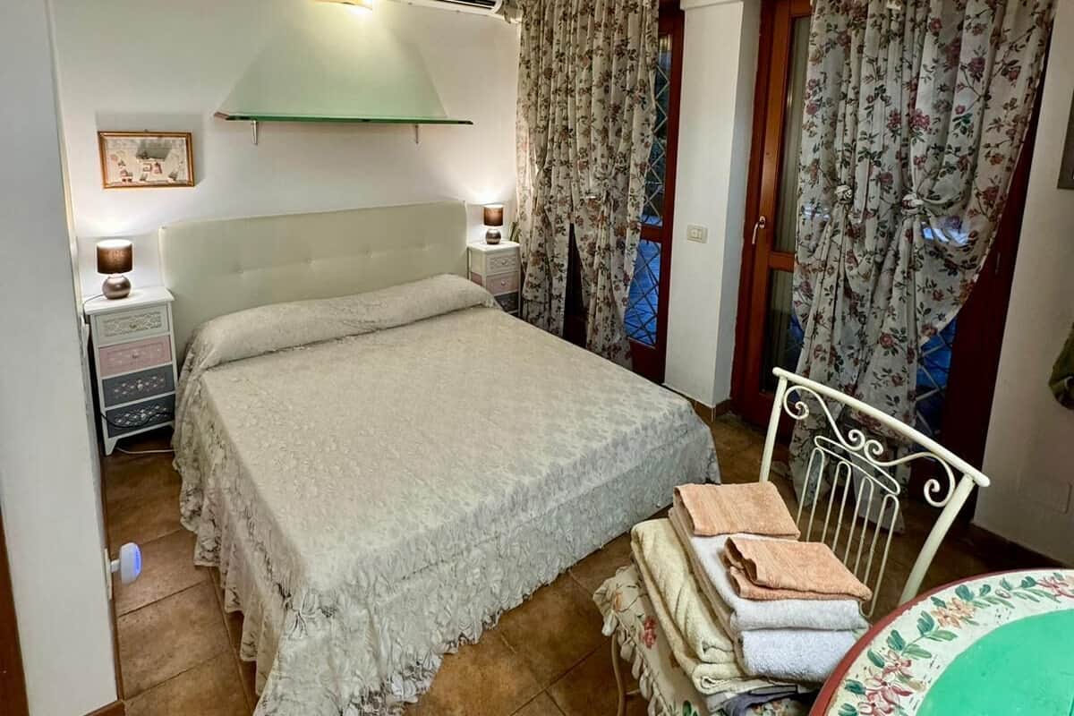 Quarto com cama, mesa de cabeceira, cadeira e mesa com toalhas.