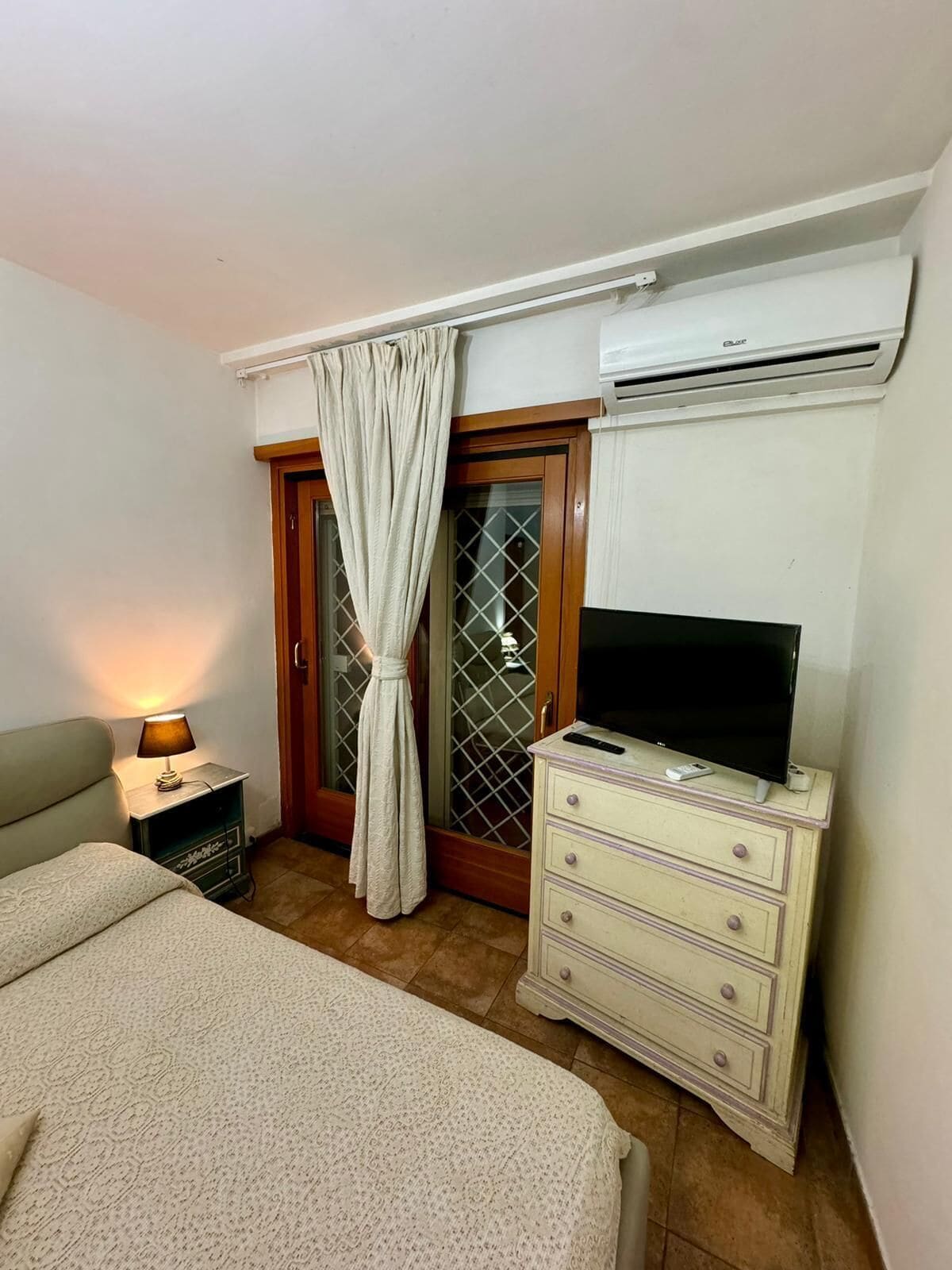 Een slaapkamer met een bed, een dressoir, een televisie en een airconditioning.