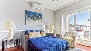 Un dormitorio con una cama grande, dos mesitas de noche, una silla, una ventana con vistas y un cuadro en la pared.