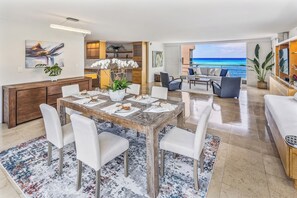 A spacious living area with a dining table set for six, a sofa, and a view of the ocean. - Oceanfront Living on the Gold Coast! (Honolulu)