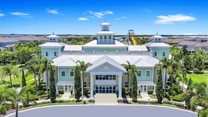 A large, multi-story building with a central entrance, surrounded by palm trees and a well-maintained lawn.