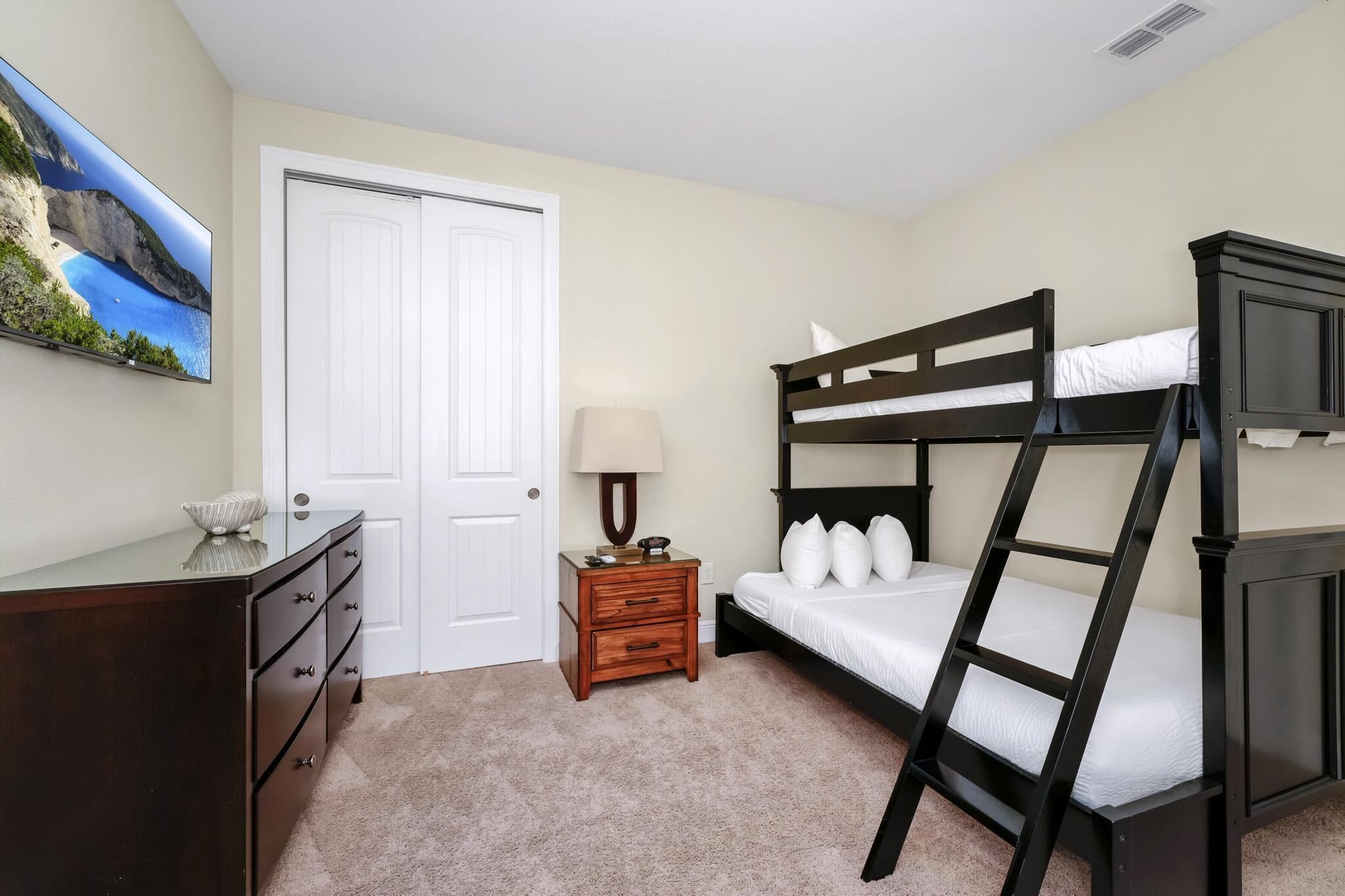 A bedroom with a bunk bed, a dresser, a nightstand with a lamp, and a painting on the wall.