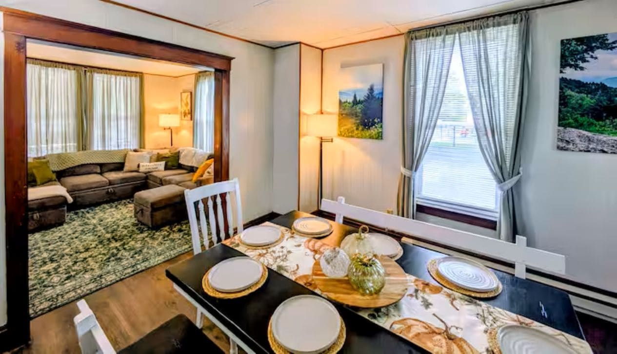 Un coin repas avec une table dressée pour quatre personnes, un canapé en arrière-plan et une fenêtre avec des rideaux.