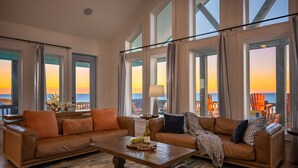 Uma sala de estar ampla com dois sofás de couro, uma mesa de centro e grandes janelas com vista para a praia.