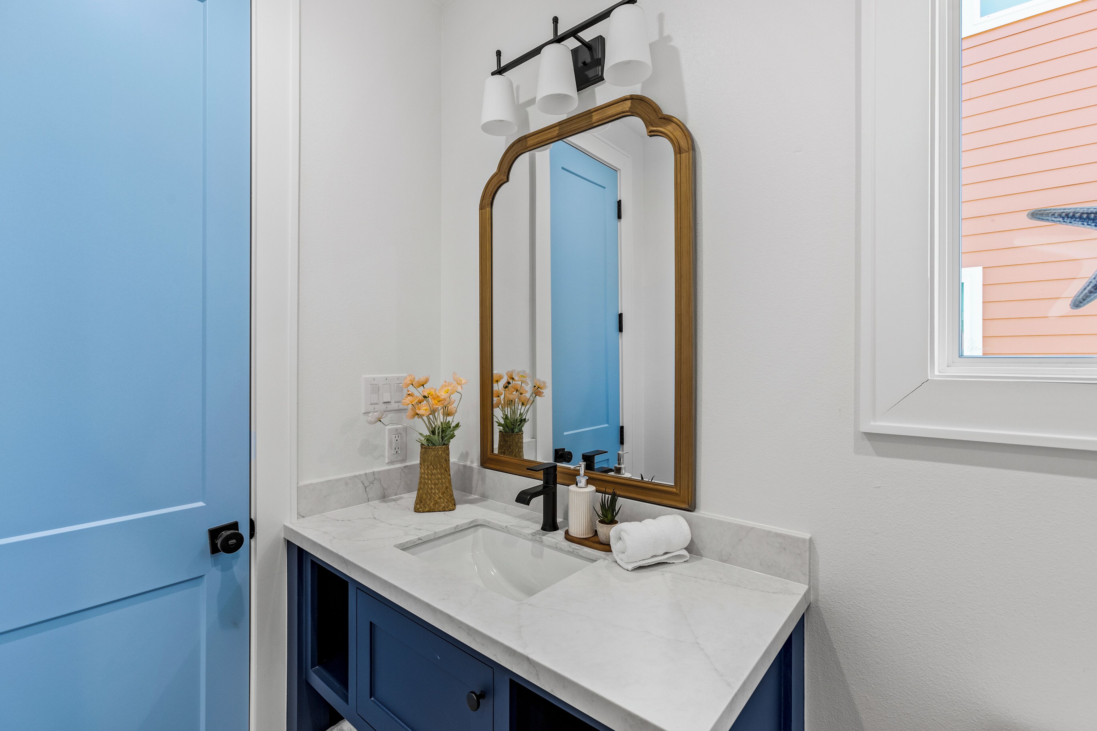 Een badkamer met een witte wastafel, een blauwe deur en een spiegel met houten lijst.