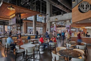A spacious cafe with high ceilings, exposed ductwork, and a mix of seating arrangements including tables and chairs.