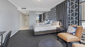 Une chambre d’hôtel avec un lit, une chaise, une petite table et une vue sur les immeubles par la fenêtre.