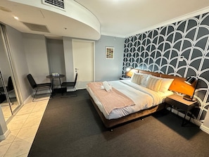 Ein Hotelzimmer mit Bett, Nachttisch, Lampe und kleinem Schreibtisch mit Stuhl.