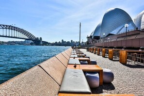 Eine Uferpromenade mit Sitzgelegenheiten und Blick auf das Sydney Opera House und die Sydney Harbour Bridge.