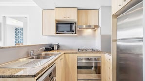A modern kitchen with a built-in microwave, stove, oven, and stainless steel refrigerator. - KozyGuru | Central Sydney | 2 Bed 2 Bath City View (Haymarket)