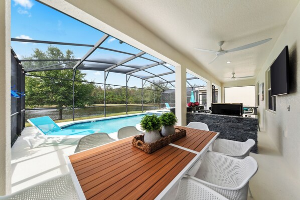 A covered outdoor area with a pool, seating, and a grill.
