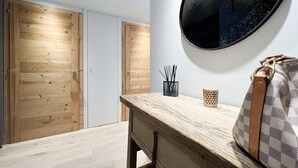 Ein Zimmer mit Holztüren, einem Holztisch, einem runden Spiegel an der Wand und einer Handtasche auf dem Tisch.