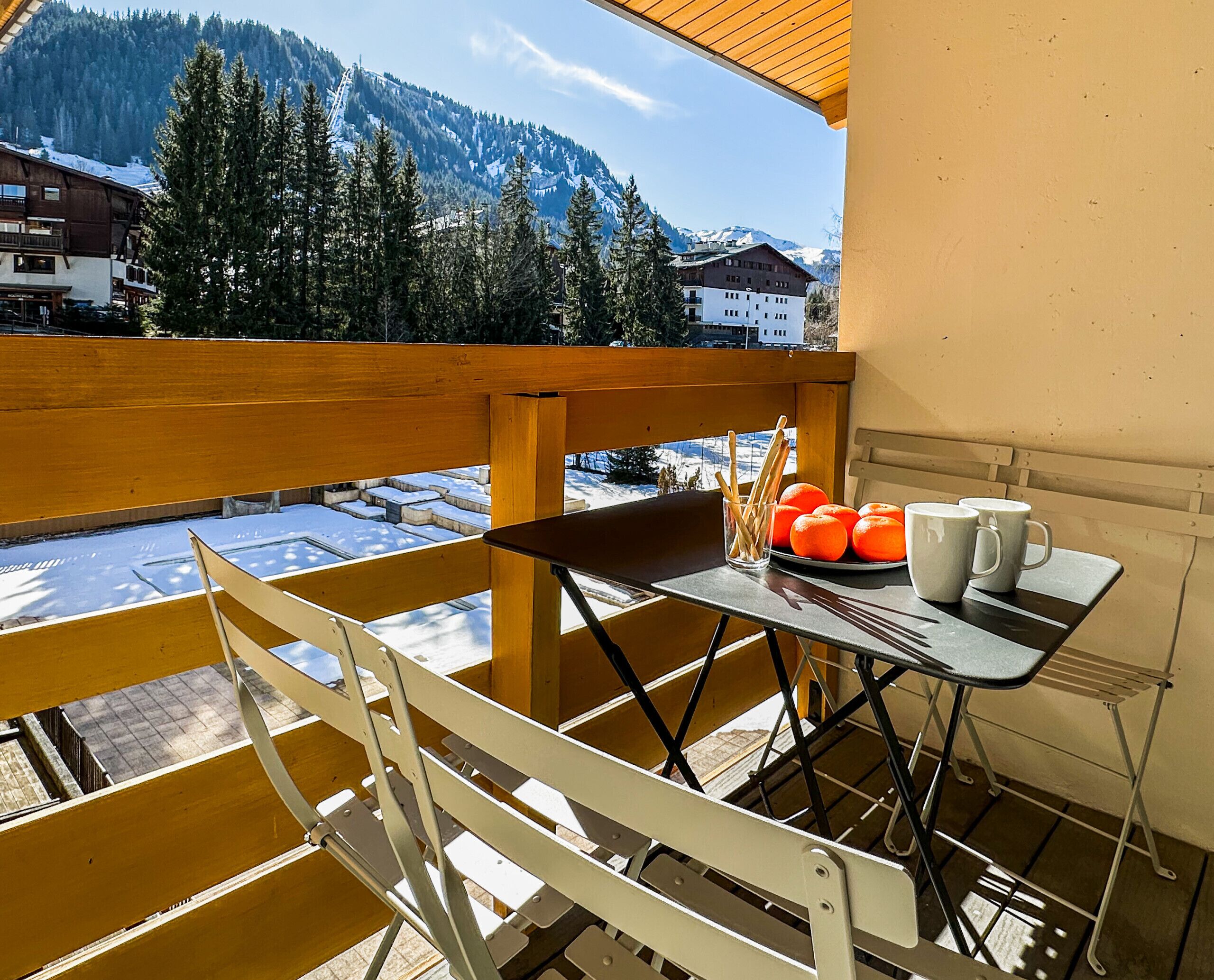 Ein Balkon mit Holzwertkasten, ein Tisch mit einer Orangenplatte, einem Glas Wasser und einer weißen Tasse.