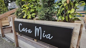 Schild für 'Casa Mia' mit einer Holzbank und Grünpflanzen im Hintergrund.