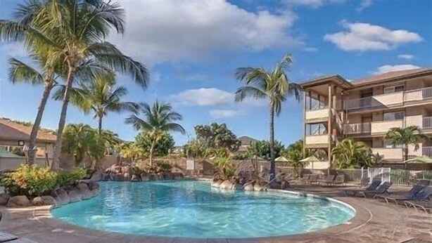 A pool surrounded by palm trees and a multi-story building with balconies.