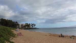 A beach with a row of buildings in the background, a sandy shore, and a cloudy sky.