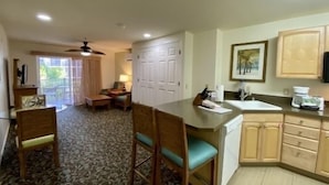 A hotel room with a dining area, a kitchen, and a sliding glass door leading to a balcony.